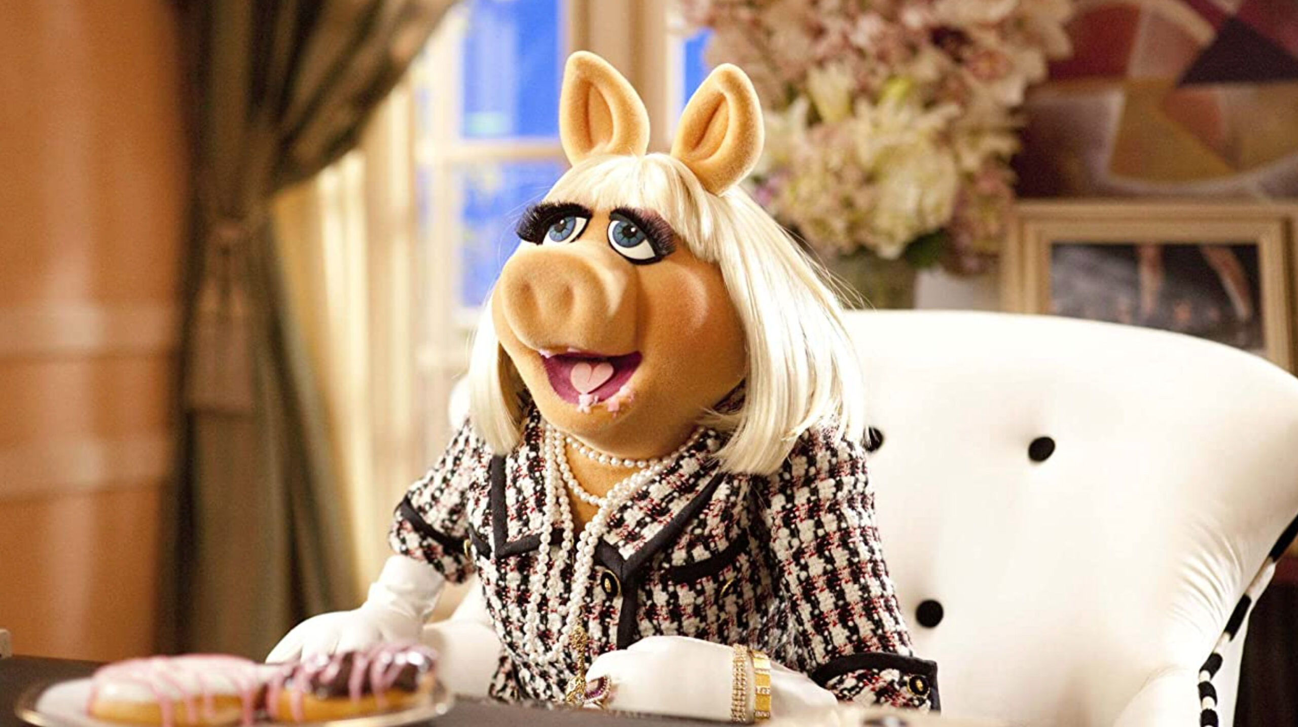 miss piggy's mouth open with donuts in her mouth. She's sitting down on a white chair.